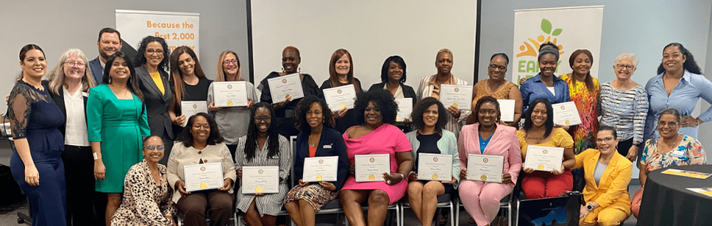 The graduating class of the ELCOC Business Institute for Early Learning Entrepreneurs smiles for the camera while holding their diplomas. The graduates are a diverse group of women and stand next to staff of the ELCOC along with the CEO Dr. Scott Fritz.