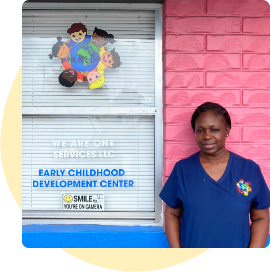 Kathy Harp stands smiling in front of her early learning center, We Are One Services. The walls are painted bright and cheerful colors.