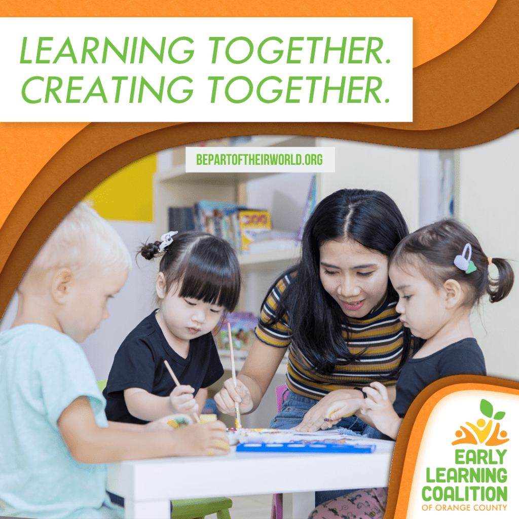Learning together. Creating together. A child care professional paints at a table with three young pre-school students. They are in a brightly lit classroom and are engaged in their artwork.