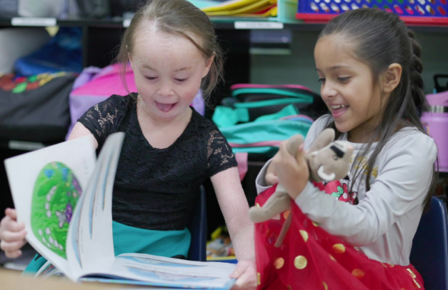 Two young girls read a picture book together in an early learning center.